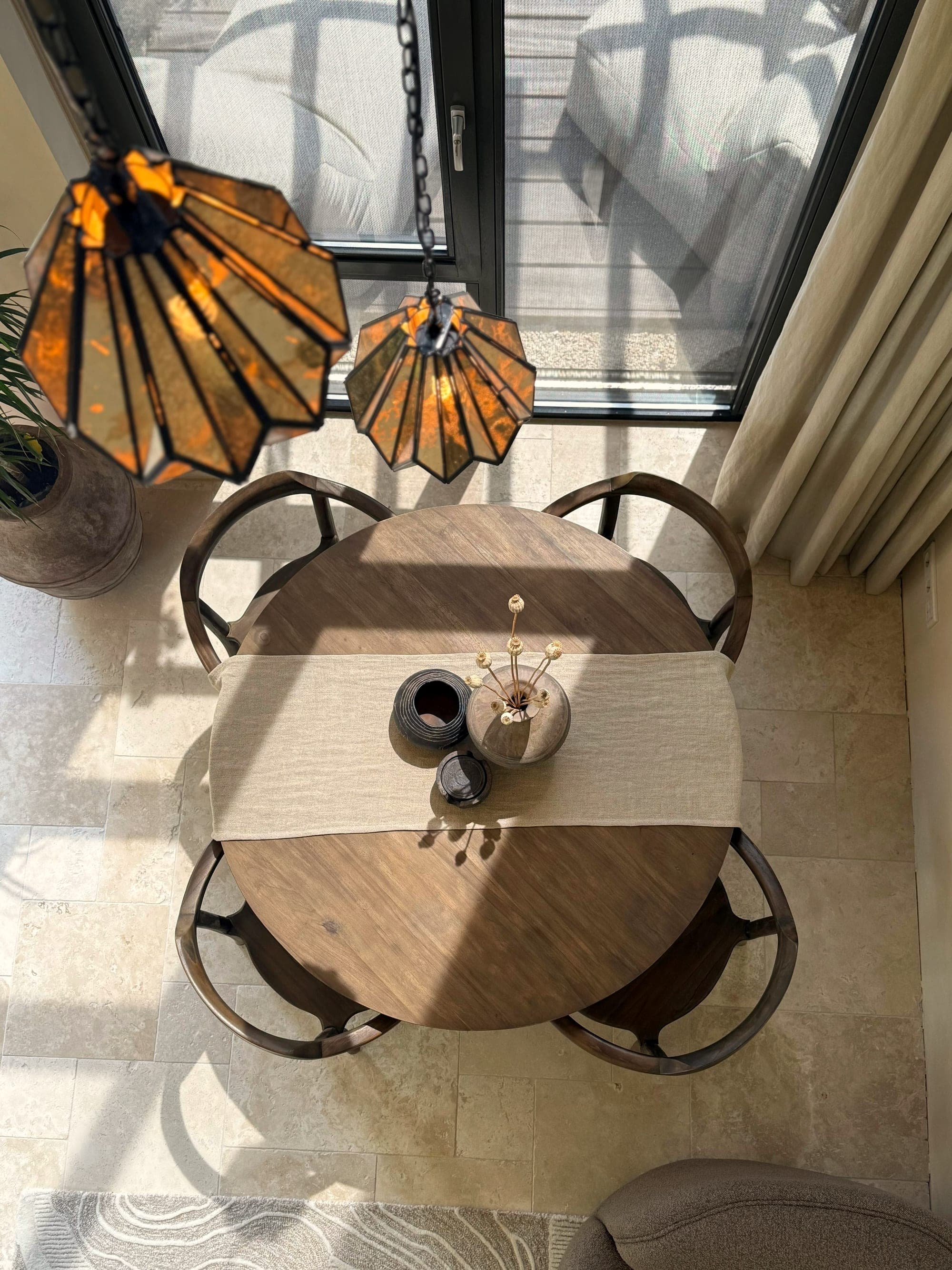 Travertin vloer in romaans verband onder een ronde eettafel met glas-in-loodlamp
