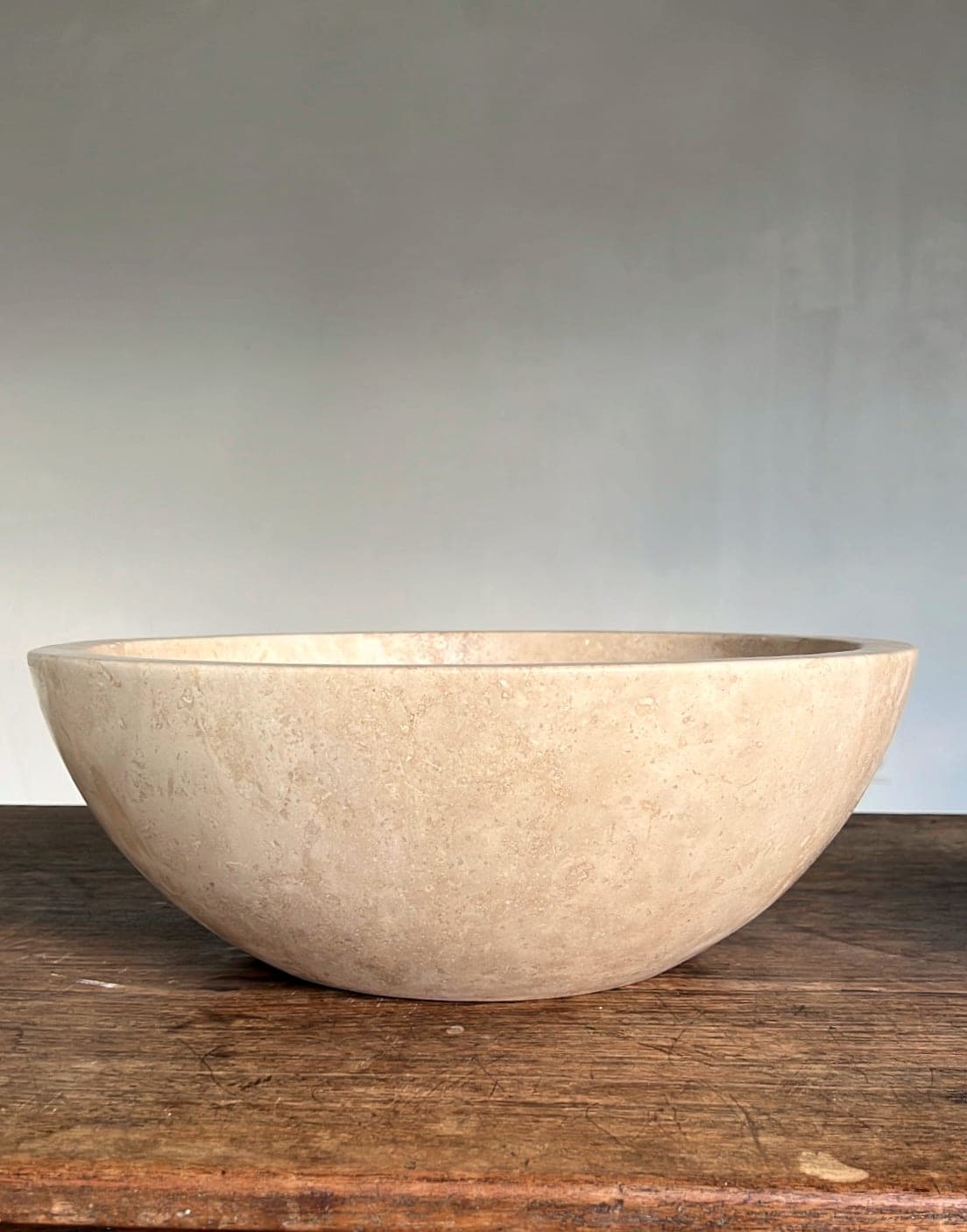 Ronde travertin schaal ø40 cm, zijaanzicht op een houten tafel